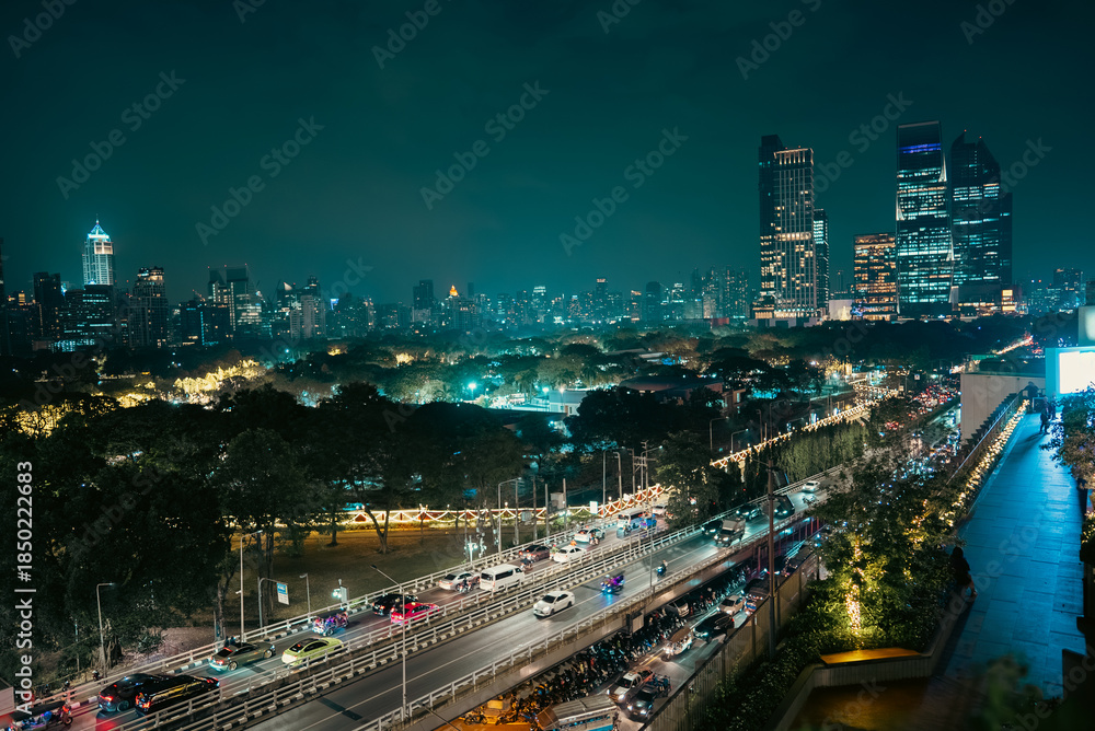 Obraz premium illuminated big city skyline at night, cars on road at rush hour, Lumpini park with festive street lights, high-rise skyscrapers and downtown glow at evening, Dusit Central, Bangkok Thailand