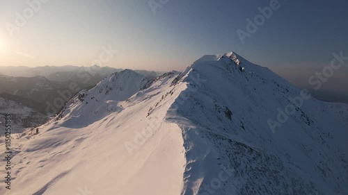 Cinematic FPV drone shot approaching mountain summit along icy ridge in early morning glow