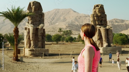 A female tourist looks at the Colossi of Memnon, a giant statue in Luxor, Egypt. An ancient historical landmark of Egypt during the time of the pharaohs.