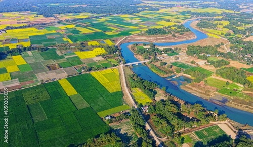 An aerial view shows a river curving through the countryside, bordered by patchwork farmland where mustard crops in full bloom