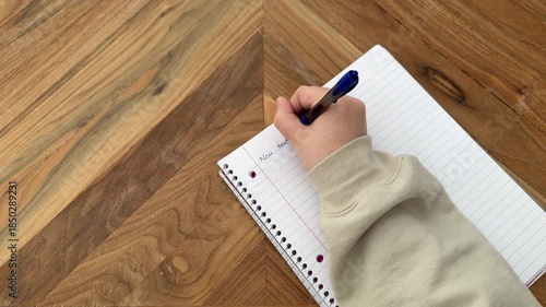 Overhead 4K video of hands writing New Year’s goals in a notebook on a wooden table. New year planning and goal setting concept.