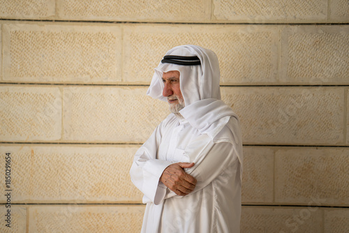 An adult Muslim man in white traditional clothes looks at the camera and expresses emotions. Elderly male sheikh on a background. High quality photo
