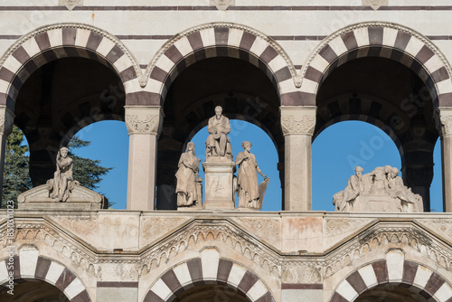 Fotografie Marble statues of allegorical figures and seated man displayed between striped arches on façade of Monumental Cemetery arcade in Milan, Italy