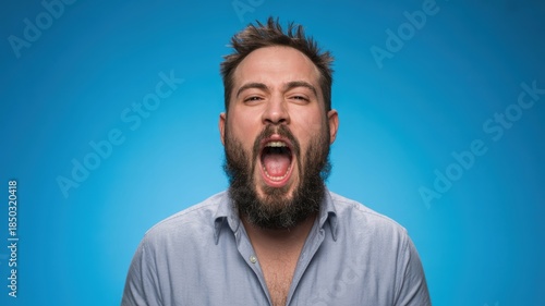 Man with Beard Screaming in Frustration with Open Mouth in Studio Shot against Blue Background for Advertising