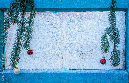festive background with a spruce branch with balls hanging on a window glass ...