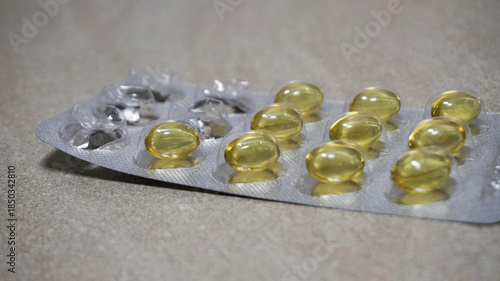 Yellow softgel capsules in blister pack on neutral background. Pharmaceutical supplements, vitamins, omega capsules, healthcare and medicine concept with copy space.
