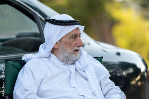 Senior arab man sitting outdoors wearing traditional arab clothing, and observing. High quality photo