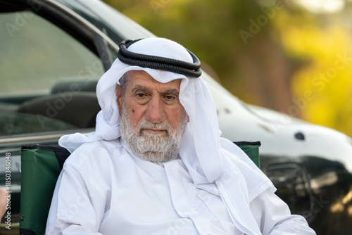 Senior arab man sitting outdoors wearing traditional arab clothing, and observing. High quality photo