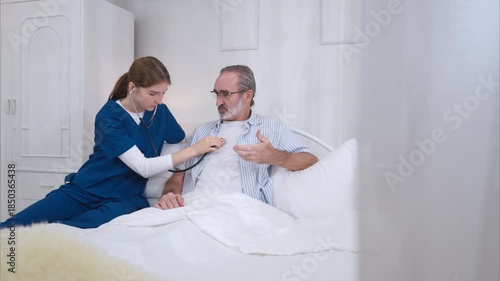 A female nurse assists an elderly patient in bed, conducts a basic health examination, and provides medical information on a digital tablet