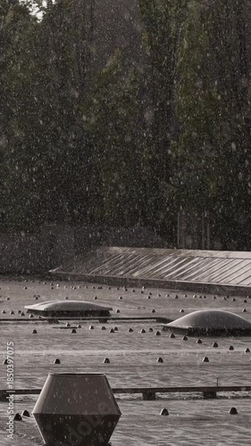 Heavy sunlit rain splashing on building roof with forest background - vertical video