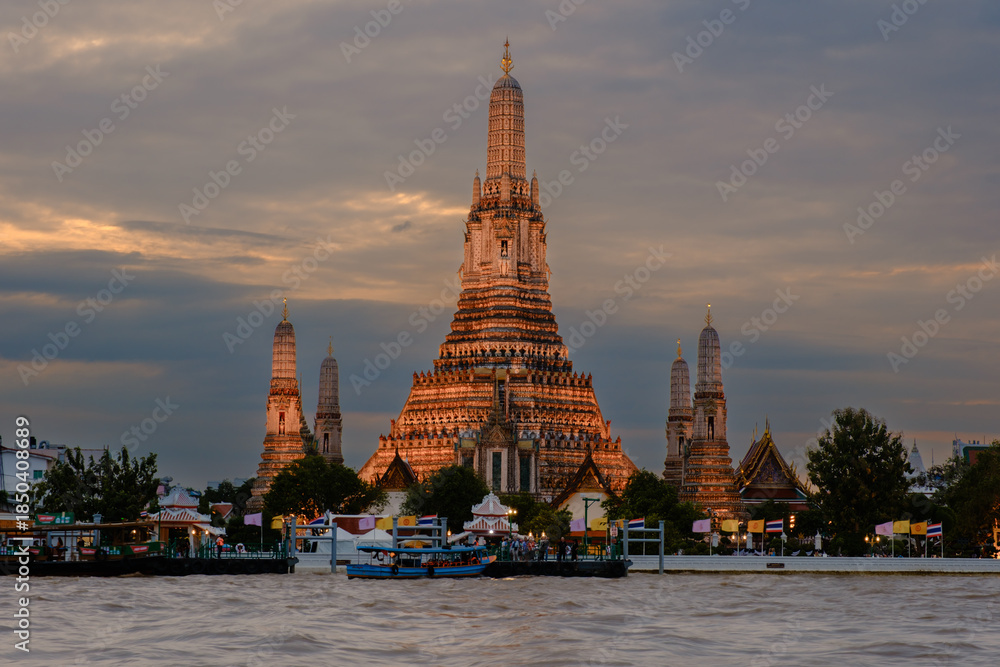 Fototapeta premium Majestic Wat Arun illuminated at dusk with the Chao Phraya River in the foreground in Bangkok