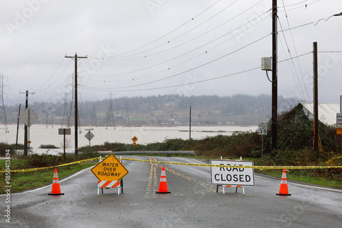 Road closed signs and caution tape warn drivers of flood water over the street preventing traffic from entering.