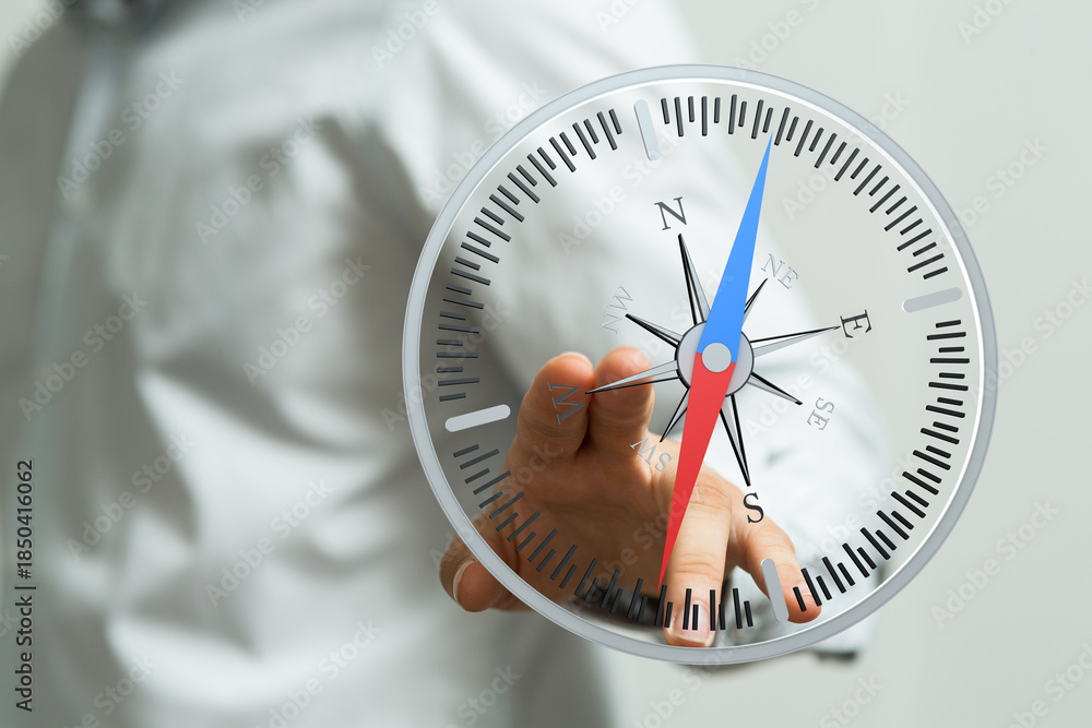 Fototapeta premium Close up of a hand holding a compass. The compass points towards the north. Navigation, direction, exploration, guidance, travel concept.