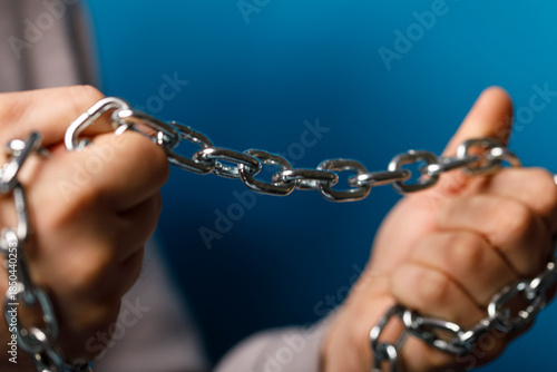 Close-up of hands pulling apart a metal chain against a blue background, representing freedom, breaking free,
