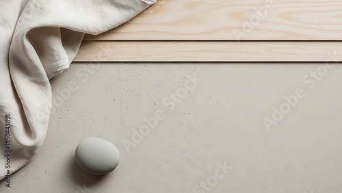 A serene, minimalist flat lay featuring a smooth grey stone, draped cream fabric, and light wood panels on a neutral beige surface, creating a calm and natural aesthetic.