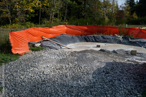 New residential housing development construction site, concrete washout and containment area with black tarp below and orange safety fencing, sunny fall day
