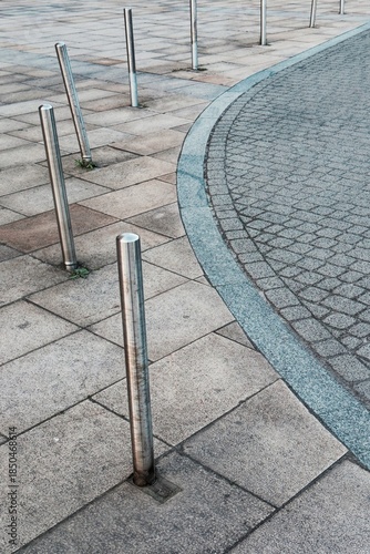 Stainless steel bollards lining a curved pedestrian walkway, modern urban design with clean lines and geometric paving.