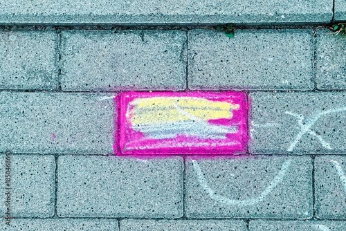 Colorful chalk drawing on grey pavement, creating a playful contrast between vibrant colors and rough urban concrete texture.