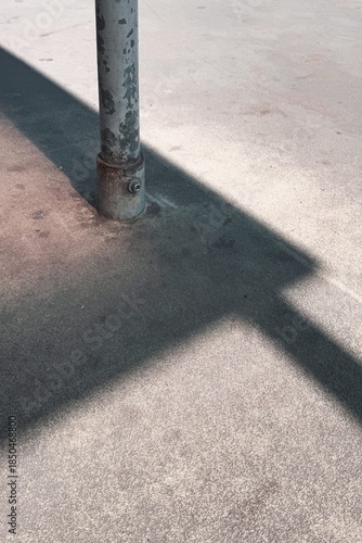 Strong diagonal shadow cast by a metal pole across a concrete surface, forming a minimalist abstract study of light and geometry.