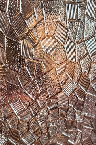 Detailed close-up of patterned glass with geometric shapes and reflective textures in warm lighting.