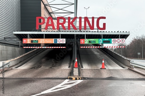 Entrance to an underground parking garage with digital signs, lane indicators, and height limit warnings on a wet roadway.