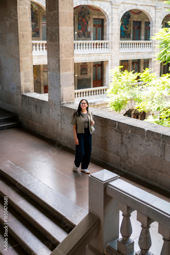 Smiling young Latin woman walking the stone corridors of Museo Vivo del Muralismo in Mexico City, enjoying the art-filled colonial architecture, wearing modern clothes, in the old SEP building.