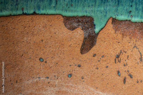 Bild auf Leinwand Macro shot of green glaze dripping over a rough terracotta pottery surface, crea