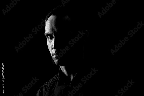 Close-up of a dramatic portrait of a mature serious guy, a musician, singer, rapper in black clothes . half a face on a black isolated background