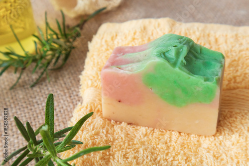 Handmade soap from natural ingredients rosemary essential oil, on yellow towel with fresh rosemary twig and loofah. Concept of sustainable use, bath products. Flat lay