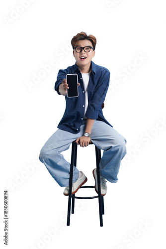 Tech Demo and Trendy Young Man: A stylish young man sits perched on a stool, showcasing a sleek, modern smartphone, offering a glimpse into the future of technology and connectivity.