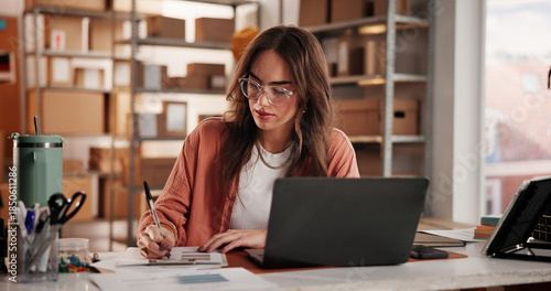 Photos Supply chain, business and woman on laptop with notebook for planning, inventory and checklist