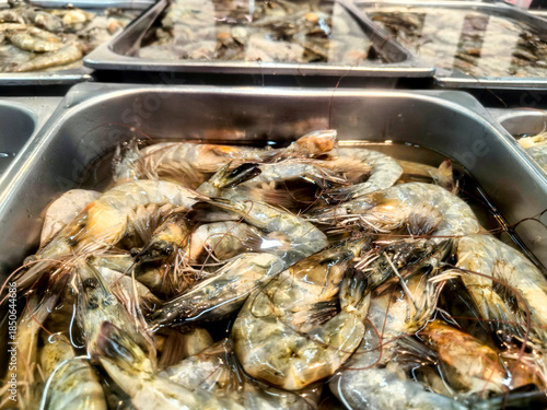 Fresh raw prawns submerged in clear water within a stainless steel tray at a seafood market.