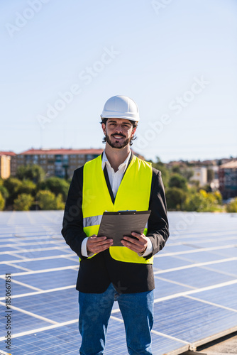 Engineer wearing hard hat and reflective vest, holding a clipboard, standing on a rooftop solar power plant, inspecting renewable energy