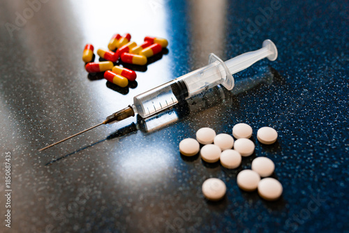 A lot of pills in a heart shape and syringe with injection on a blue background as a symbol of medical treatment. Choice antibiotics against vaccine from Covid-19. Emergency help in case heart attack