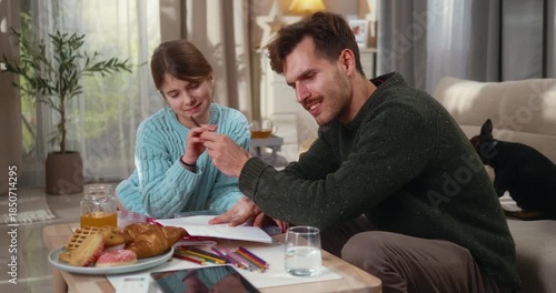 Father and mother help their daughter with homework in a warm, modern living room. Caring parents, learning together, and a cozy family moment at home.
