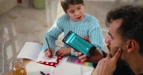 Father holds a smartphone using an AI chat app to help his daughter with homework. Modern learning, technology support, and family education at home.