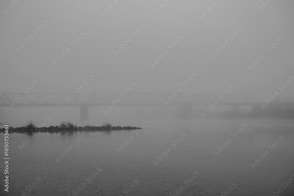 Fototapeta premium Nebel über dem Fluss und einer Brücke in einer Stadt am Abend