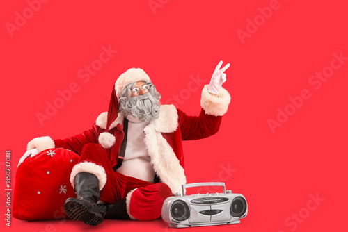 Santa Claus with bag full of gifts and boombox sitting on red background