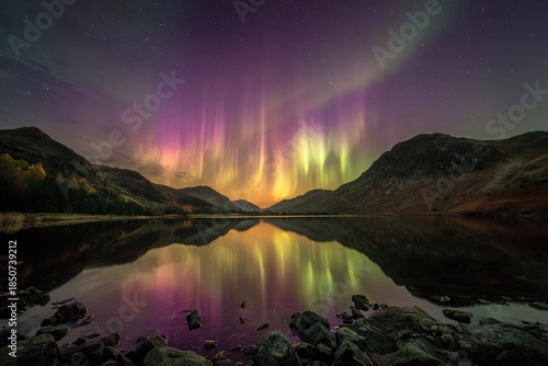 Colorful lights display over mountains and lake at night with stars in the sky