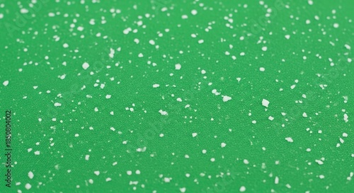 Tiny white particles scattered across a vibrant green textured surface, creating a subtle pattern.