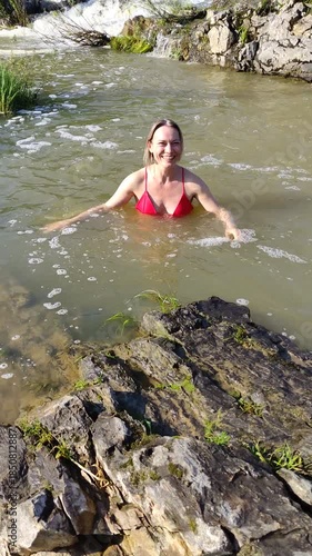 Beautiful adult slender woman in a red swimsuit is bathing in a small waterfall.