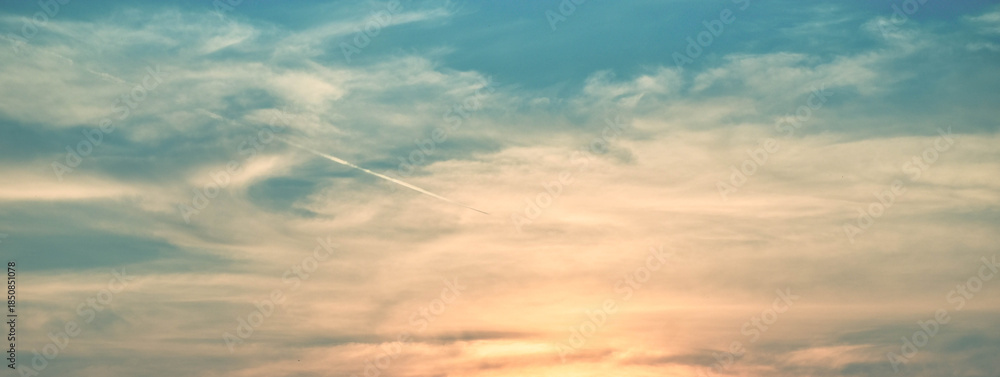 Fototapeta premium A trail of smoke from a jet aircraft is heading low to the right of the image. The cloudy sky in the image is blue-yellow.