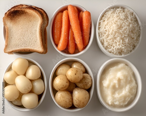 A variety of bland diet foods like toast, carrots, rice, eggs, potatoes, and mashed potatoes are arranged in small white bowls.
