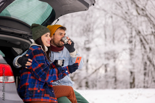 Couple using smart phone and drinking tea while taking winter vacation road trip break