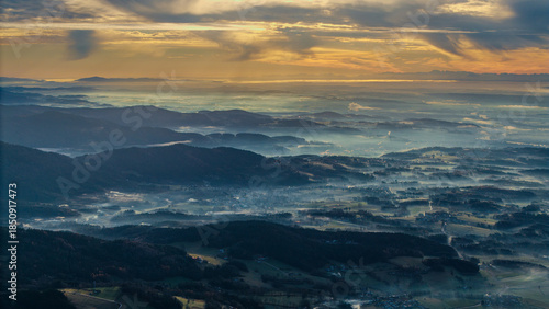 Blick auf das Tal bei Sonnenaufgang mit Nebel und den Ostalpen in der Ferne