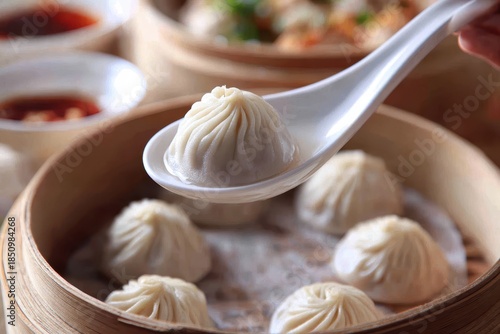 Close-up of a perfectly pleated Xiao Long Bao soup dumpling lifted from a steaming bamboo basket.