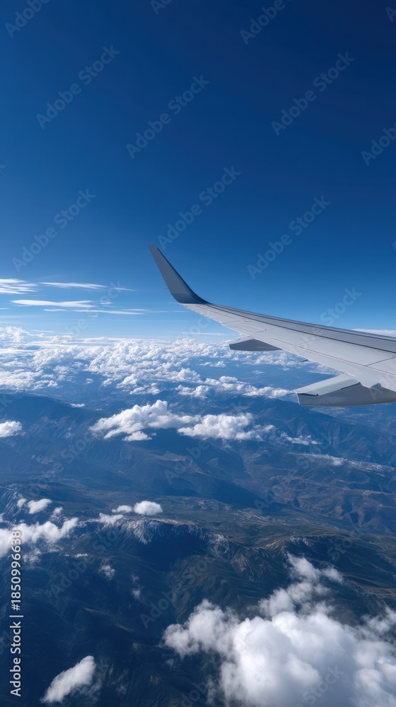 Fototapeta premium Airplane Wing Against Clear Blue Sky Over Clouds and Mountains in Bright Daylight