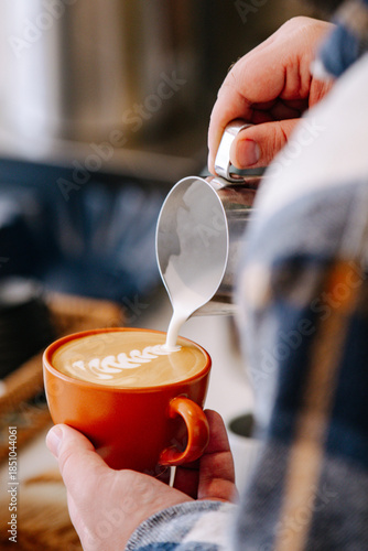 Barista pouring steamed milk into coffee cup to create latte art. Close-up of hands making cappuccino in a cozy cafe