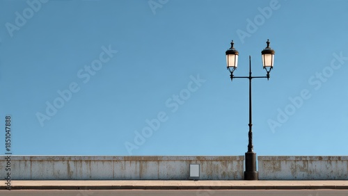 Architectural shot of a classic black double-arm street lamp standing beside a weathered concrete wall and sidewalk under a bright, clean blue sky with vast copy space.