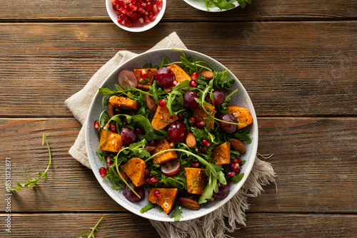 Fresh salad with roasted pumpkin and grapes on plate wooden surface